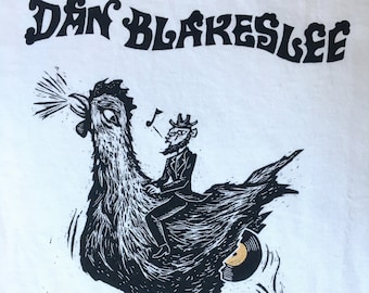 Dan Blakeslee unisex tshirt with a chap riding a chicken laying gold records handmade handprinted homemade