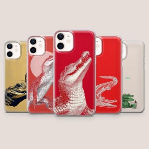 Peut inclure: Cinq coques de smartphone avec des illustrations de crocodiles. Une est jaune avec un crocodile noir, deux sont rouges avec des dessins de crocodiles blancs, une est rouge avec un crocodile blanc, et une est transparente avec un petit crocodile vert et le texte bite.