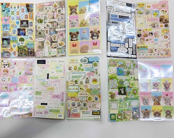 May include: A collection of ten rectangular sticker sheets featuring various colorful designs, including cartoon characters, small icons, floral patterns, and Japanese text. The sheets are arranged in two rows, displaying a variety of themes and styles.