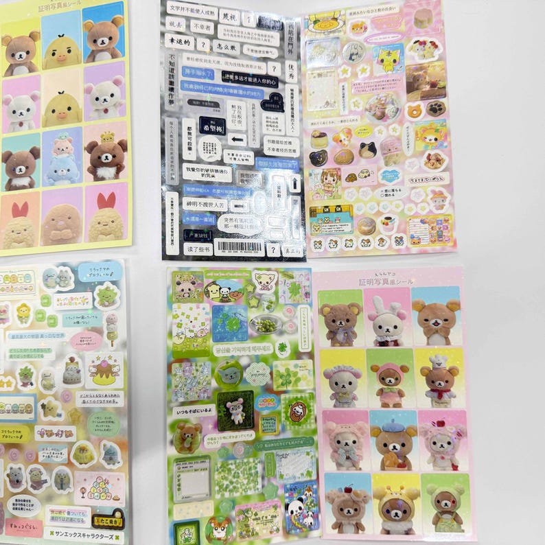 May include: A collection of five sticker sheets featuring various cartoon characters, including Rilakkuma bears and small creatures. The sheets display diverse designs such as grid-based character portraits, text-heavy labels, and assorted decorative icons in multiple colors.