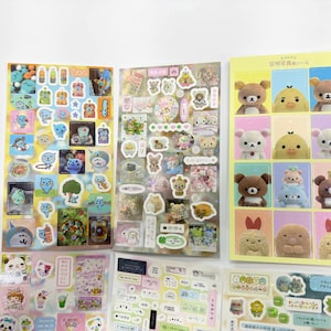 May include: Five sheets of decorative stickers featuring various cartoon characters, including bears, birds, and small creatures. The designs include individual character portraits, food items, and small icons in pastel and vibrant colors on clear backgrounds.
