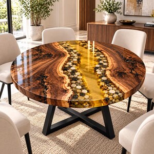 Puede incluir: Una mesa de comedor redonda con un tablero de madera de borde natural y un diseño de río central relleno de piedras de río lisas y multicolores incrustadas en resina transparente de color ámbar. La mesa tiene una base de metal negro en X.