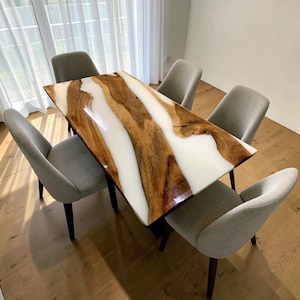 Puede incluir: Una mesa de comedor rectangular que presenta una losa de madera natural con un borde vivo prominente y una incrustación de resina blanca brillante, acompañada de seis sillas tapizadas en gris claro con patas de madera oscura.