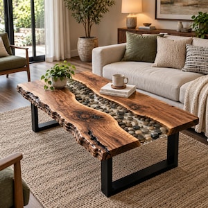 May include: A rectangular coffee table featuring a live edge wood slab with a central river-like inlay filled with smooth, multi-colored river stones encased in clear resin, supported by two sturdy black metal U-shaped legs.