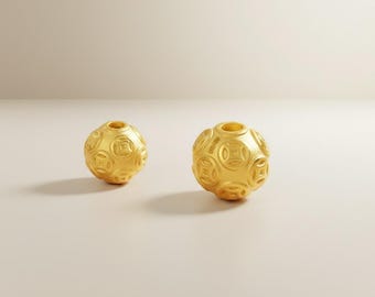May include: Two gold-colored, spherical beads with a textured surface. Each bead features a series of embossed, circular designs. The beads are displayed on a neutral background, highlighting their metallic sheen and intricate detailing. The beads are likely jewelry components.