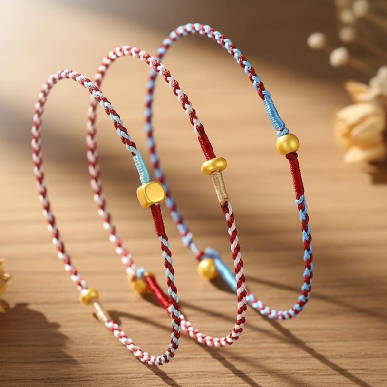 Puede incluir: Pulseras trenzadas en rojo, blanco y azul con detalles dorados. Las pulseras presentan un dise&ntilde;o tejido con peque&ntilde;as cuentas doradas y piezas cil&iacute;ndricas doradas. Las pulseras son probablemente para usar en la mu&ntilde;eca.