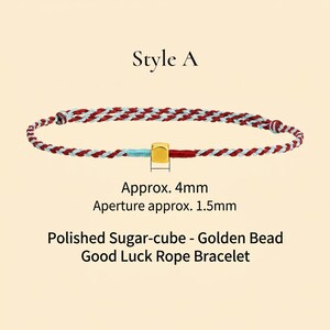 Puede incluir: Una pulsera de cuerda trenzada con hilos rojos, blancos y azules, con una cuenta c&uacute;bica dorada. La pulsera est&aacute; etiquetada como "Style A" y mide aproximadamente 4 mm. El texto dice "Polished Sugar-cube - Golden Bead Good Luck Rope Bracelet."