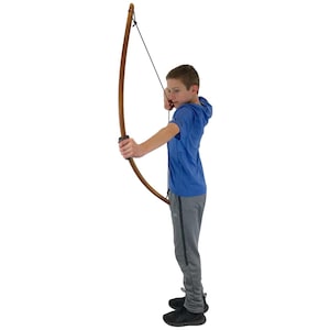 May include: A wooden bow with a black string is held by a person wearing a blue hooded shirt and gray sweatpants. The bow is curved and has a dark brown finish. The person is aiming the bow.