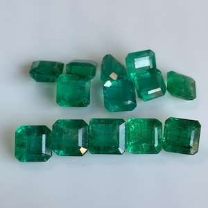 May include: A collection of emerald gemstones, each with a vibrant green hue. The stones are cut into various shapes, including rectangular and faceted forms, showcasing their clarity and brilliance. The gemstones are displayed against a white background.