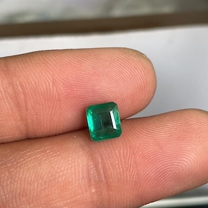 May include: A vibrant, emerald-green gemstone cut into a rectangular shape with faceted edges. The stone displays a deep, saturated green hue and clear internal clarity, reflecting light across its polished, geometric surface.