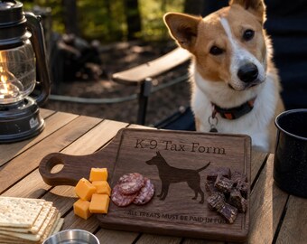 May include: A wooden serving board with the text "K-9 Tax Form" and a dog silhouette, alongside cheese, crackers, salami, and dog treats. A dog is looking at the camera. A lantern and a metal bowl are also on the wooden table.