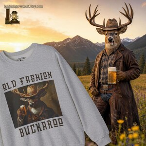 May include: A light gray crewneck sweatshirt featuring a graphic print of a deer wearing a cowboy hat and holding a beer mug, with the text "OLD FASHION BUCKAROO" printed in dark brown block letters above and below the central illustration.