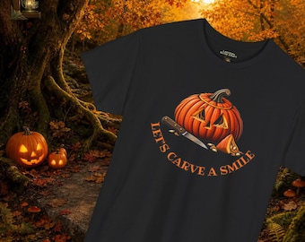 May include: A black short-sleeved t-shirt featuring a graphic of an orange jack-o'-lantern with a carving knife and a pumpkin slice. The text "LET'S CARVE A SMILE" is printed in orange below the pumpkin illustration on the front of the shirt.
