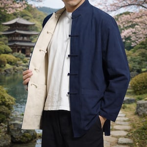 May include: A navy blue reversible jacket with a mandarin collar and toggle closures. The jacket's interior is a light beige color. The jacket is worn over a white t-shirt. The background features a Japanese garden with a pagoda and cherry blossoms.