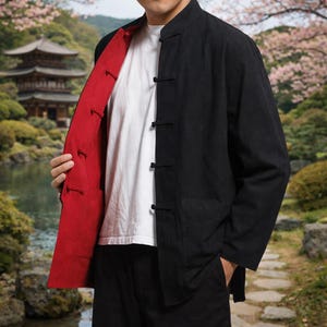 May include: Black jacket with a red lining, featuring a mandarin collar and frog closures. The jacket is worn over a white t-shirt. The style is reminiscent of traditional Asian garments. The jacket has two pockets.