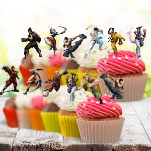 May include: A collection of cupcake toppers featuring various Street Fighter characters in dynamic action poses, including Ryu, Chun-Li, and Akuma, designed to be inserted into cupcakes with pink and white frosting in paper liners.