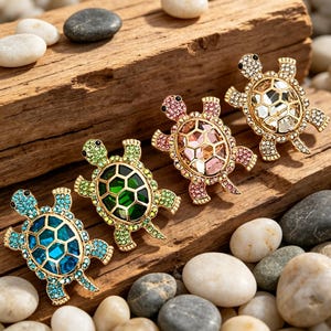Könnte beinhalten: Vier mit Juwelen besetzte Schildkrötenbroschen in Blau, Grün, Rosa und Gold. Jede Schildkröte hat einen goldfarbenen Rahmen und ist mit farbigen Edelsteinen besetzt. Die Broschen sind auf einem verwitterten Holzstück ausgestellt.