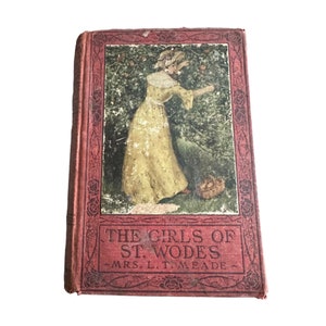 May include: A vintage book titled "The Girls of St. Wodes" by Mrs. L.T. Meade. The cover features a woman in a yellow dress picking apples from a tree.