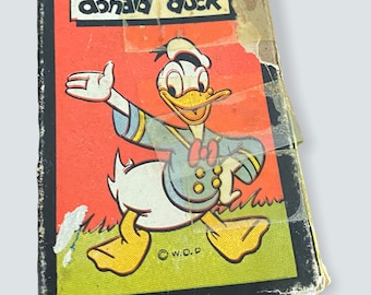 May include: Vintage "Donald Duck" book cover featuring Donald Duck in a blue sailor suit with a red bow tie, set against a red and green background. The title "donald duck" is printed at the top. The cover shows signs of wear.