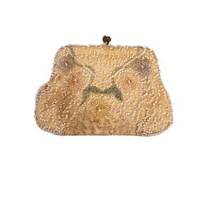 May include: A vintage beaded clutch purse with a floral design. The purse is made of a light beige fabric and is decorated with white and pink beads. The purse has a clasp closure and a small handle.