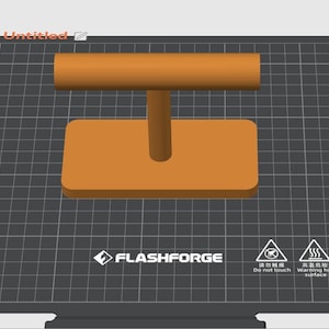 May include: An orange 3D-printed object, possibly a handle or support, is centered on a dark gray grid. The object has a rectangular base, a vertical post, and a horizontal bar. The Flashforge logo and warning symbols are visible.