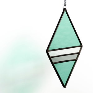 Geometric, modern stained glass suncatcher made with green, grey and clear wavy textured glass. Made in the Tiffany Glass style and with black patina. Hangs on a black chain on a white background to show color and texture of glass art. Side view.