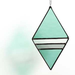 Geometric, modern stained glass suncatcher made with green, grey and clear wavy textured glass. Made in the Tiffany Glass style and with black patina. Hangs on a black chain on a white background to show color and texture of glass art.