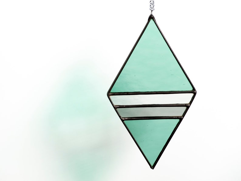 Geometric, modern stained glass suncatcher made with green, grey and clear wavy textured glass. Made in the Tiffany Glass style and with black patina. Hangs on a black chain on a white background to show color and texture of glass art.