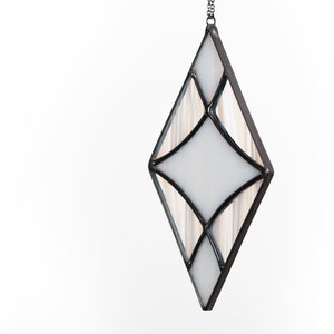 Curved design stained glass suncatcher made with opaque white and wispy white and clear glass. Made in the Tiffany Glass style and with black patina. Hangs on a black chain on a white background to show color and texture of glass art.