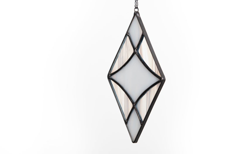 Curved design stained glass suncatcher made with opaque white and wispy white and clear glass. Made in the Tiffany Glass style and with black patina. Hangs on a black chain on a white background to show color and texture of glass art.