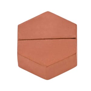Op de afbeelding: Een terracotta-kleurig zeshoekig object met een horizontale gleuf die over het midden loopt. Het item heeft een plat bovenoppervlak en schuine zijkanten, wat een geometrische vorm presenteert met een matte afwerking en een consistente roodbruine tint.