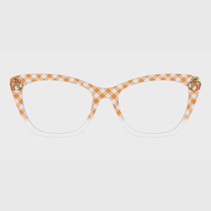 May include: Cat-eye glasses featuring an orange and white gingham check pattern across the frame. Each outer corner of the frame is decorated with a small, detailed illustration of a pumpkin with a green stem and a small bow.