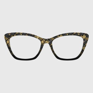 May include: Cat-eye glasses featuring a black frame with a detailed pattern of gold and black tropical leaves and foliage. The lenses are clear and the frame has a distinct pointed outer edge, showcasing a botanical design across the entire surface.