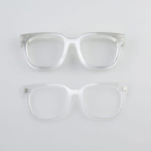 May include: Two pairs of clear, square-framed spectacles are shown against a white backdrop. The spectacles have a classic, minimalist design, with a transparent appearance. The frames are made of a clear material, and the lenses are empty.