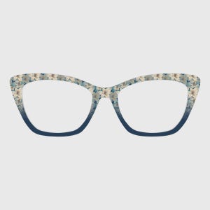 Puede incluir: Gafas de ojo de gato con un estampado floral en la parte superior de la montura que se transforma en un color azul oscuro sólido en la parte inferior. El diseño floral presenta pétalos claros sobre un fondo suave, creando un degradado.