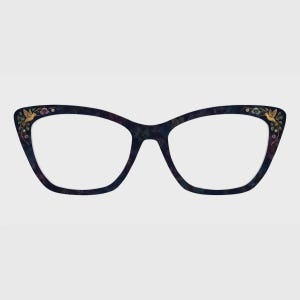 May include: Cat-eye glasses featuring a dark navy blue frame with a subtle floral pattern. The outer corners of the frame are decorated with small, detailed illustrations of golden hummingbirds surrounded by tiny pink and blue flowers.