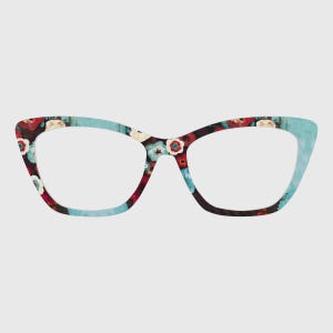 Puede incluir: Gafas de ojo de gato con un estampado floral. Las monturas presentan una mezcla de flores rojas, azules y blancas sobre un fondo oscuro, con acentos azul claro en los bordes exteriores. Las lentes son transparentes.