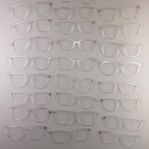 May include: A collection of clear, transparent eyeglasses frames in various styles. The frames are arranged on a white surface, showcasing different shapes, including rectangular, round, and cat-eye designs. The glasses are made of a clear material.
