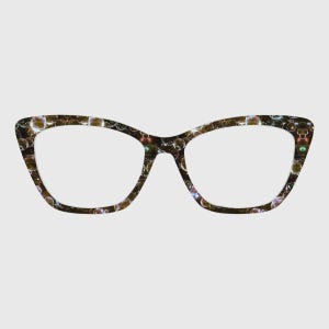 Puede incluir: Gafas de estilo ojo de gato con montura estampada. La montura presenta un fondo oscuro con un patrón de burbujas en tonos dorados, marrones y otros colores. Las lentes son transparentes.