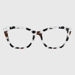 May include: Cat-eye shaped eyeglasses featuring a distinct cow-print pattern across the frame. The design consists of irregular black and brown patches set against a white background, creating a bold, high-contrast look for these spectacles.
