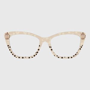 Puede incluir: Gafas de estilo ojo de gato con montura color crema con un sutil estampado de leopardo. Los bordes inferiores están adornados con lunares negros. Pequeñas ilustraciones de tazas de té de burbujas están en las esquinas superiores de la montura.