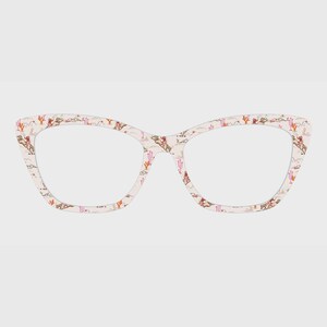 May include: Cat-eye glasses frames with a light cream background featuring a repeating pattern of small brown horses, riders, and pink cacti. The frames have a distinct upswept shape at the outer corners and a smooth, matte-finish surface.