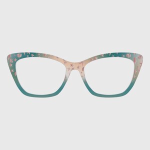 Puede incluir: Gafas de estilo ojo de gato con montura degradada de color turquesa a beige. La montura está decorada con un estampado de estrellas y conchas rosas. Las lentes son transparentes.