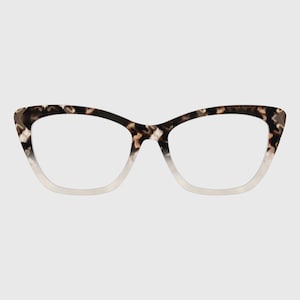 Op de afbeelding: Cat-eye bril met een bruin en zwart schildpadpatroon op het bovenste frame dat overgaat in een transparant materiaal aan de onderkant. Het montuur heeft een opvallende, omhooglopende vorm bij de buitenste hoeken en heldere glazen.