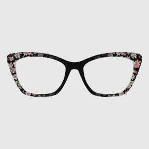May include: Black cat-eye eyeglasses with a floral pattern in pink, white, and gray. The frames have a classic shape with a bold black bridge and temples. The lenses are clear.