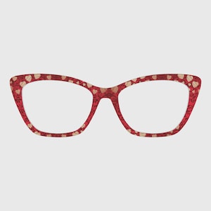 May include: Red cat-eye eyeglasses with a repeating gold heart pattern. The frames have a decorative floral design and are a stylish accessory. The lenses are clear, and the glasses are set against a neutral background.