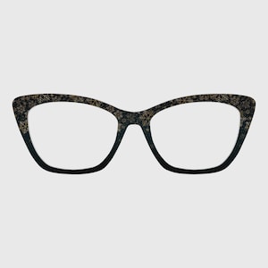 May include: Cat-eye glasses featuring a black frame with a gold snowflake pattern. The design transitions from a dense gold snowflake print along the top rim to a solid black finish at the bottom of the lenses, creating a distinct contrast.