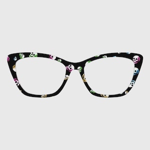 May include: Black cat-eye glasses with a repeating pattern of colorful skulls. The frames have a classic shape with a modern, edgy design. The skulls are in various colors, including pink, green, and blue.