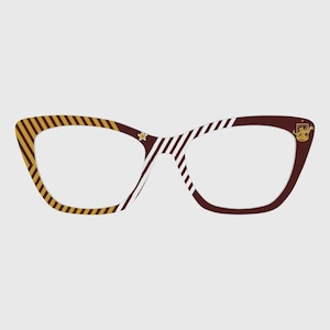 May include: Cat-eye style eyeglasses with a brown frame, featuring gold and white striped accents. The left side has gold stripes, while the right side has white stripes. A gold star and crest detail the frame.
