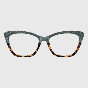 May include: Stylish cat-eye glasses. The upper part of the frames has a textured grey-blue pattern, contrasting with the tortoiseshell pattern on the lower half. The lenses are clear. A contemporary and fashionable eyewear choice.